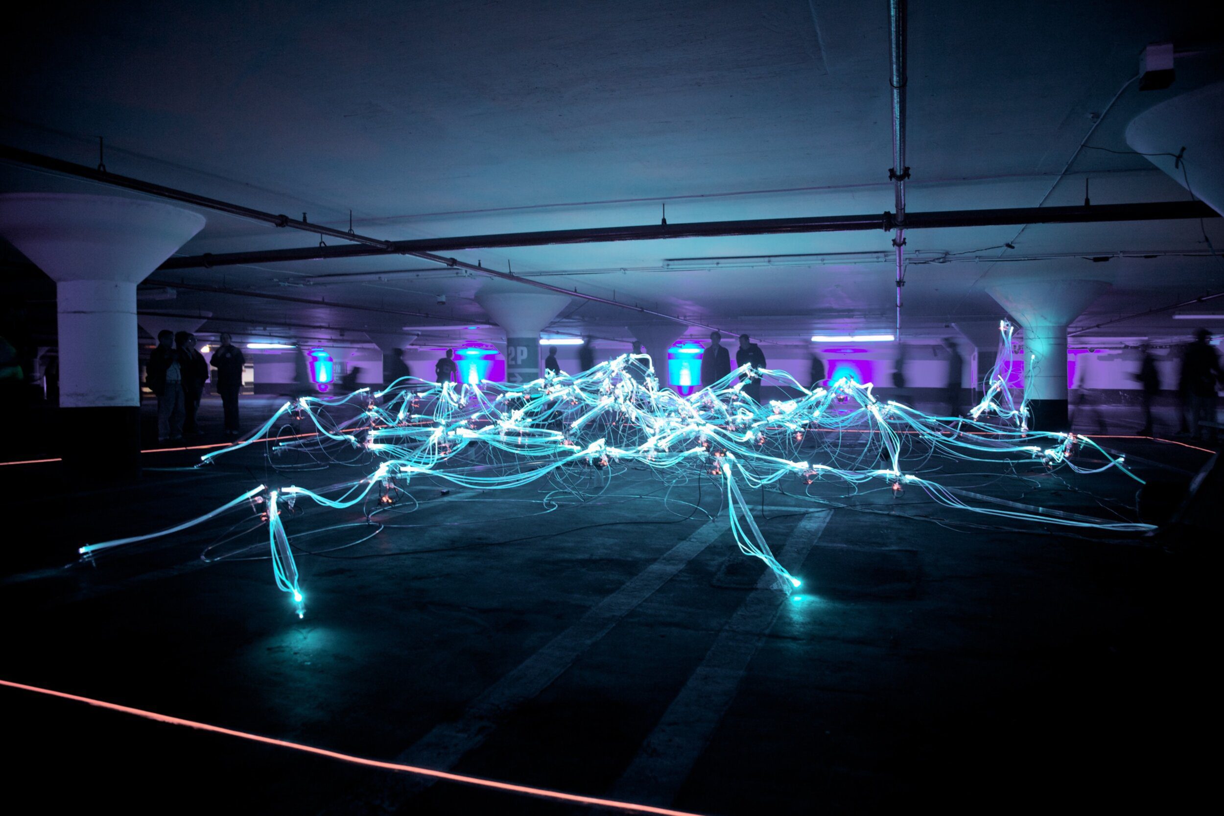 Light installation in dark car park with people watching on