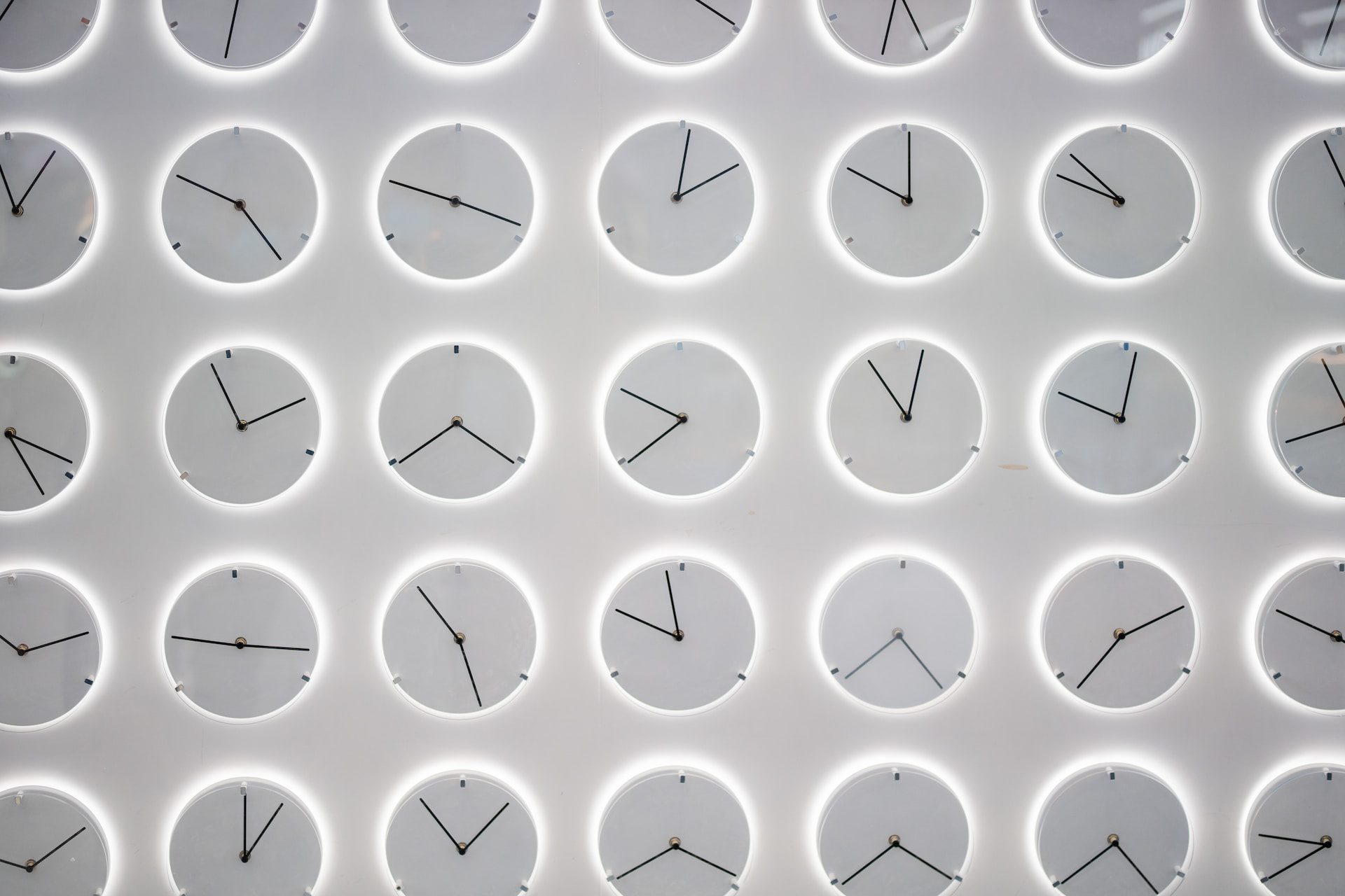 White wall covered in uniform white clocks all showing different times