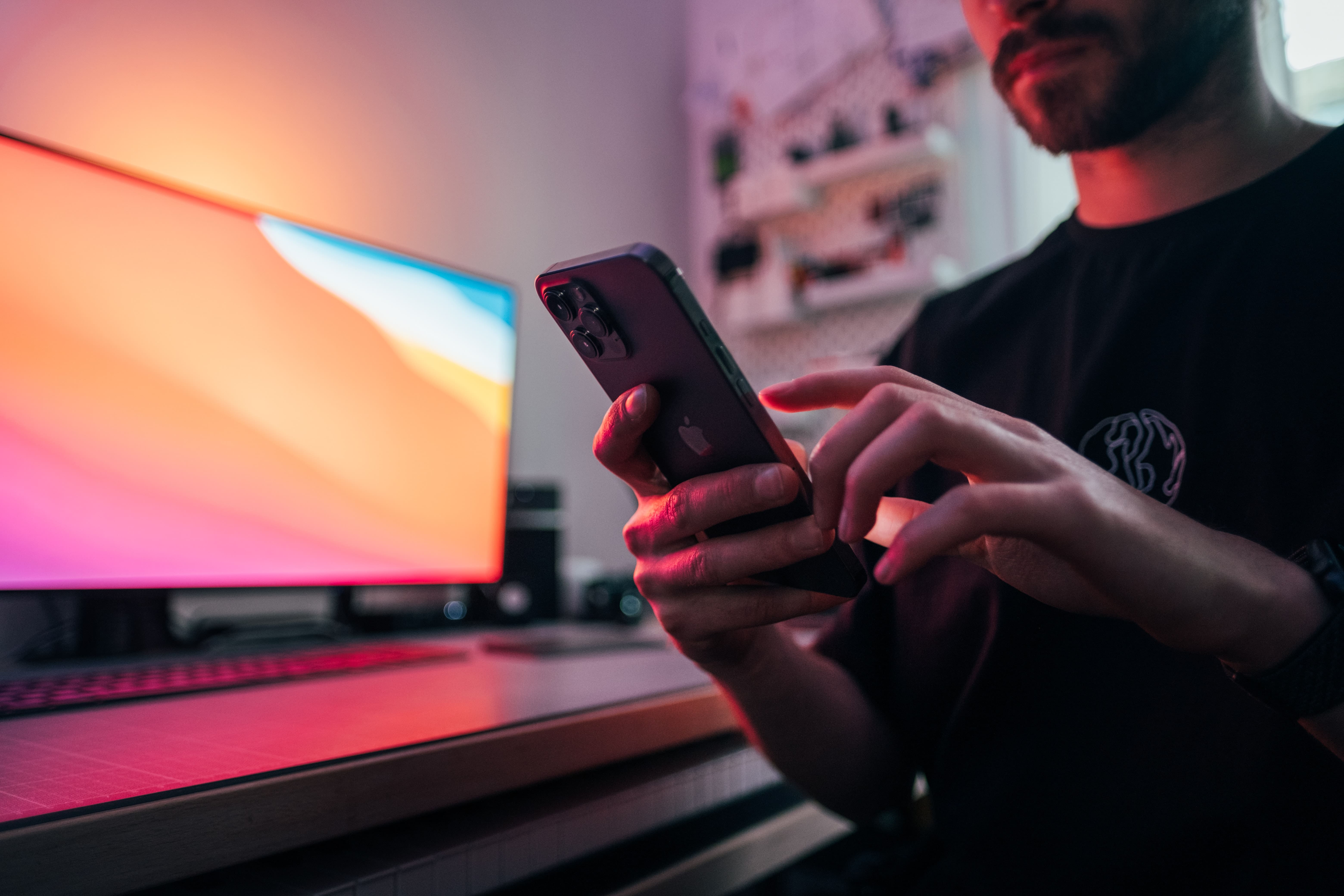 Man looking at iPhone with bright monitor in background